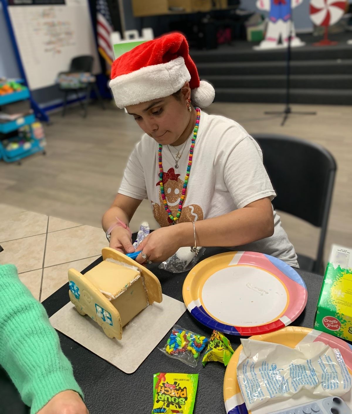 A woman wearing a santa hat is making a gingerbread house