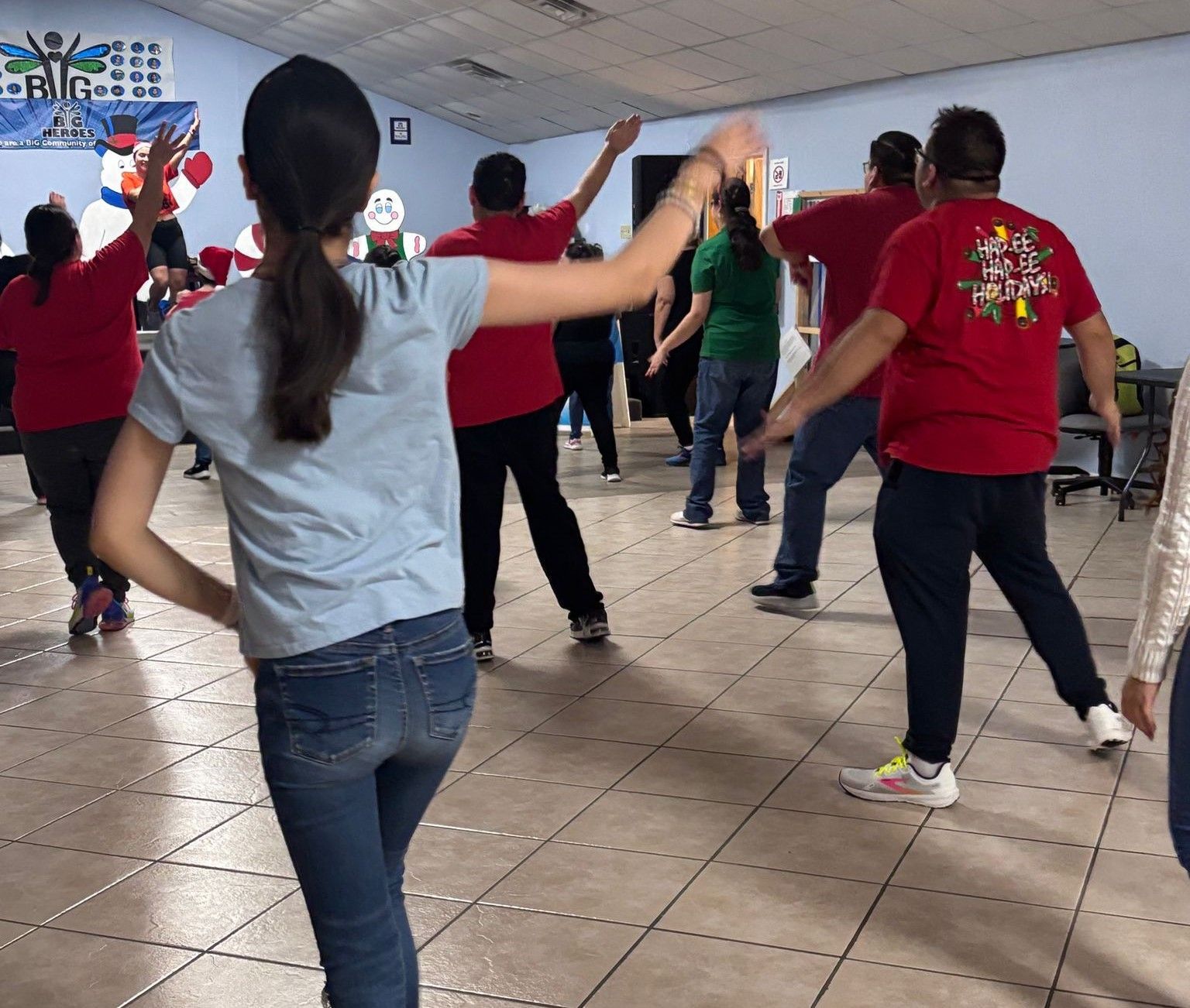 A group of people are dancing in a room and one of them is wearing a red shirt with a snowflake on it