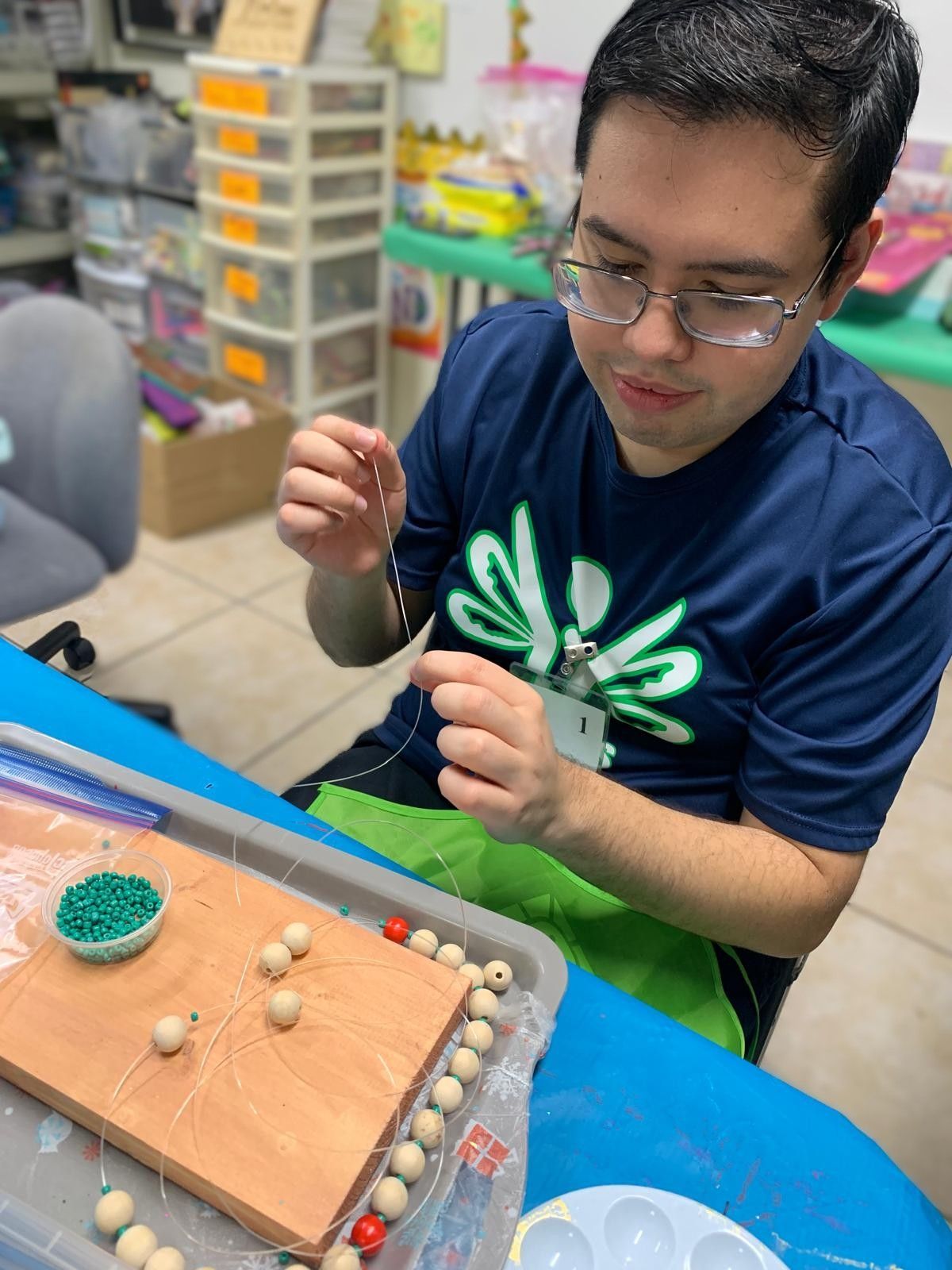 A man is sitting at a table making a necklace with beads.