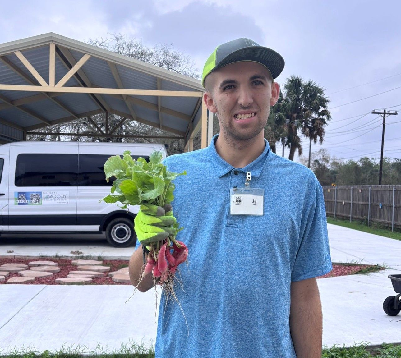 A man in a blue shirt is holding a bunch of radishes