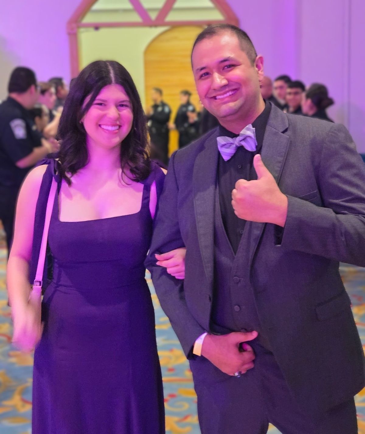 A man in a suit is giving a thumbs up next to a woman in a purple dress