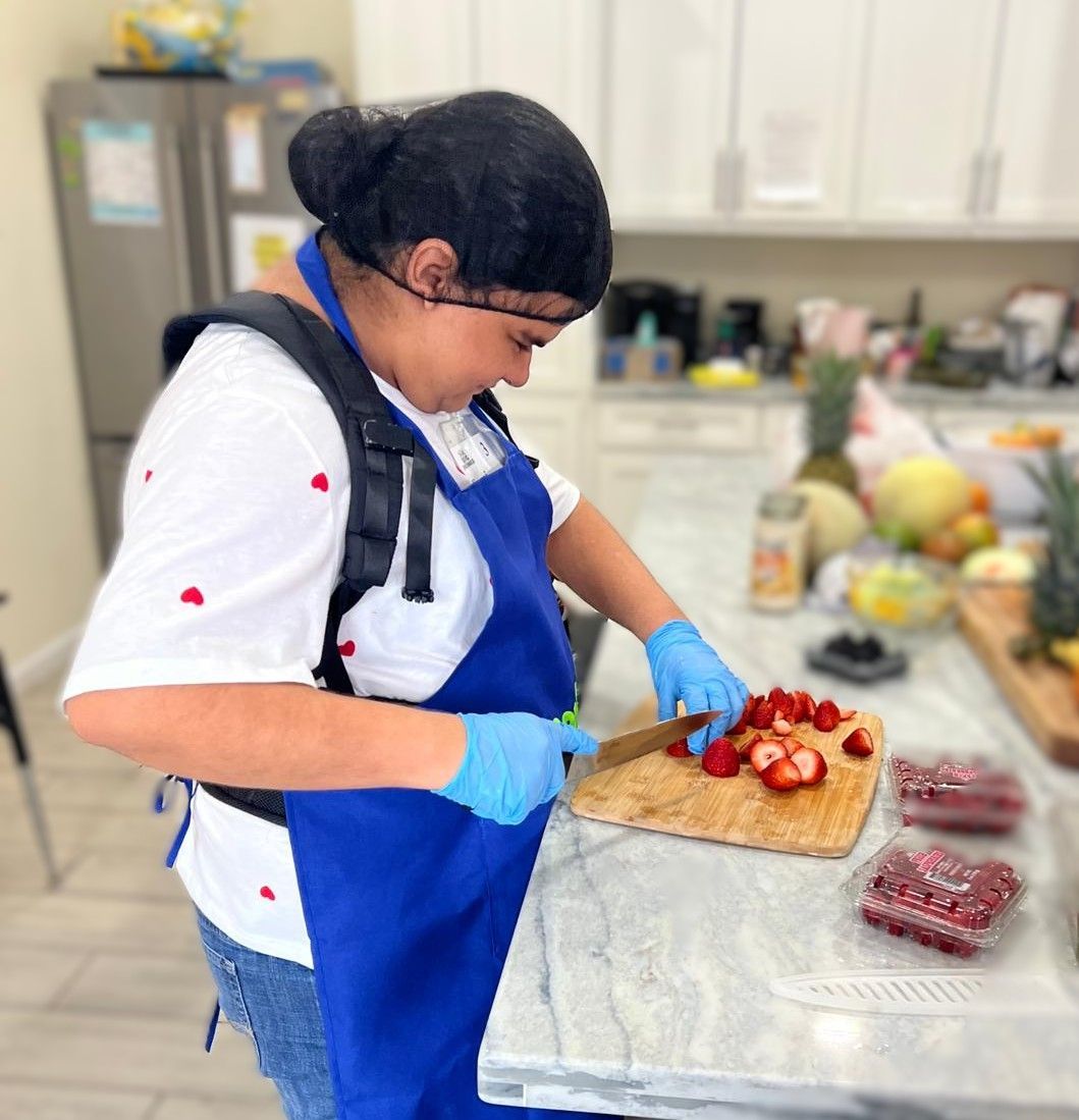A woman in a blue apron is cutting strawberries on a cutting board
