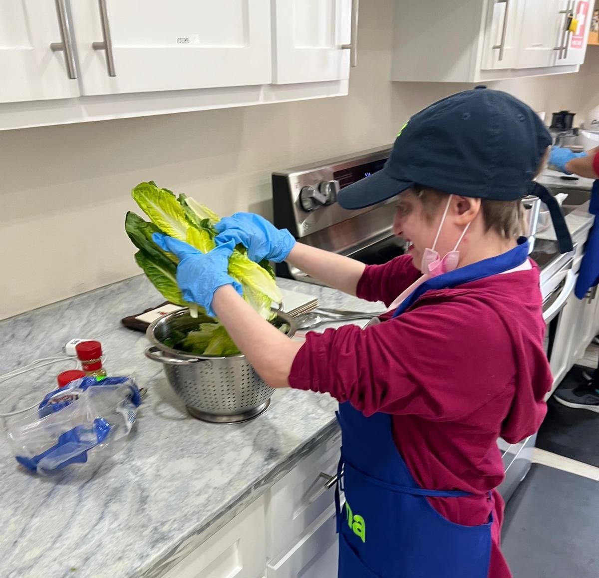 A woman in a blue apron is washing lettuce in a kitchen