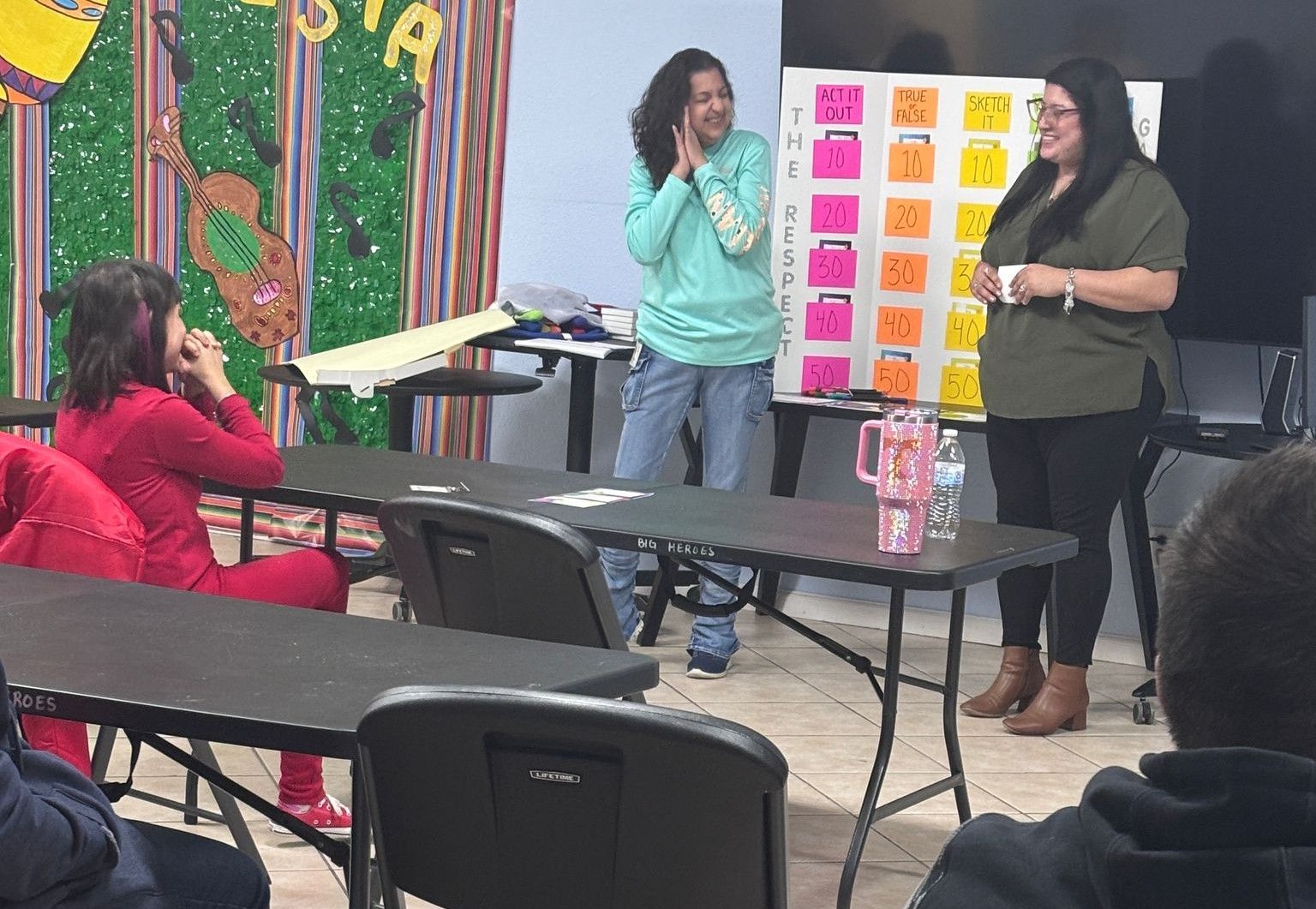 Two women are standing in front of a group of people in a classroom.