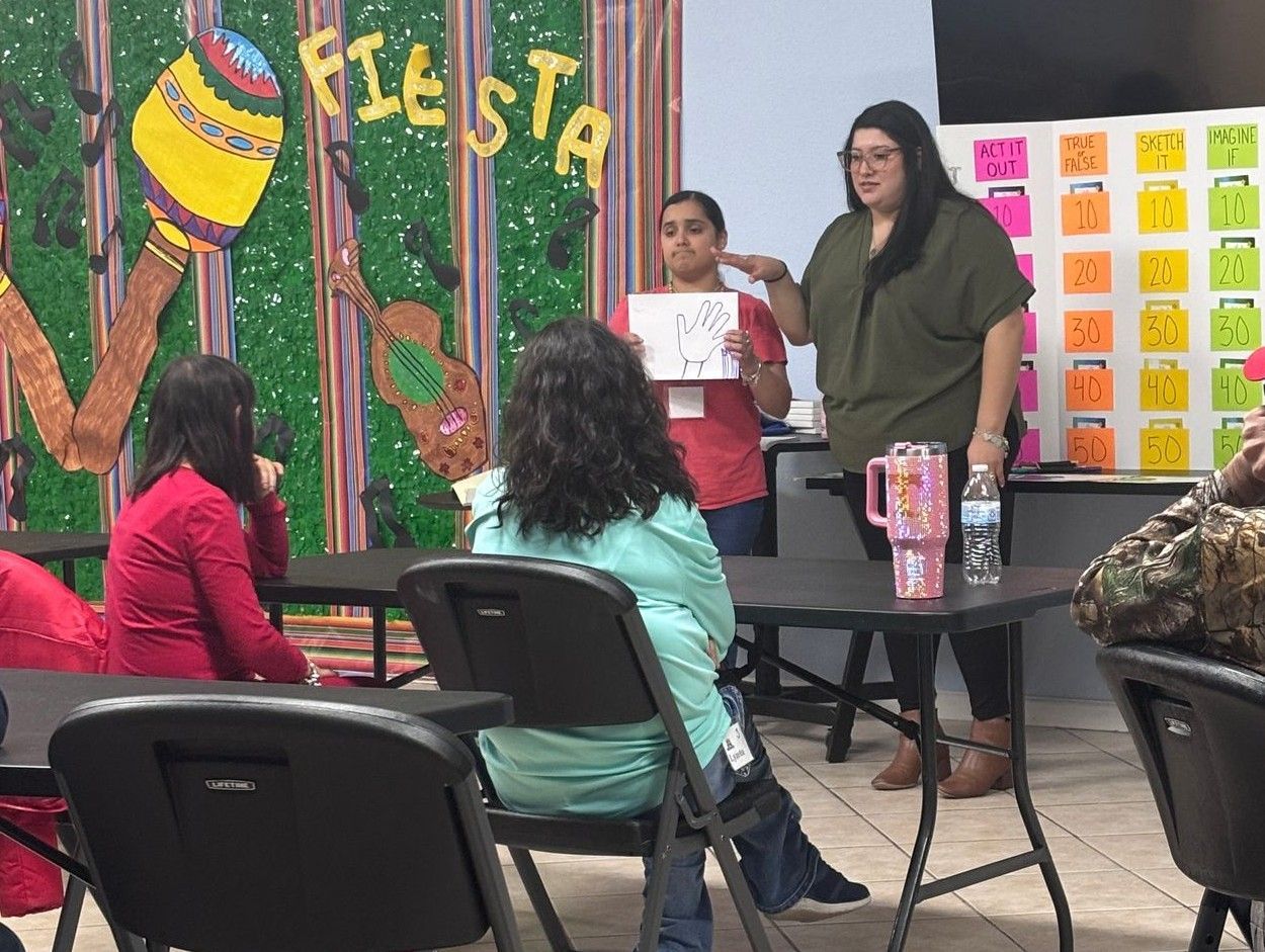 A group of people are sitting at tables in front of a wall that says fiesta.