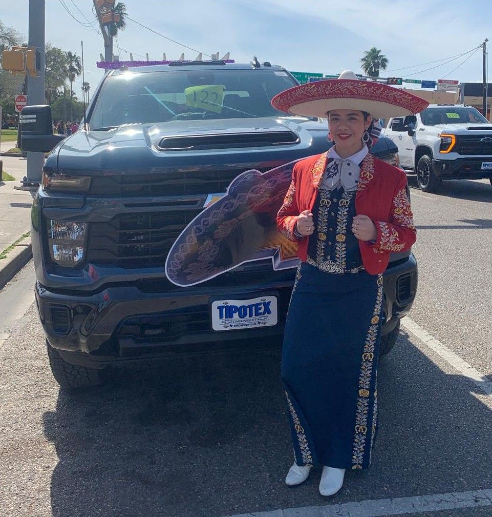 A woman in a mariachi outfit is standing in front of a typex truck