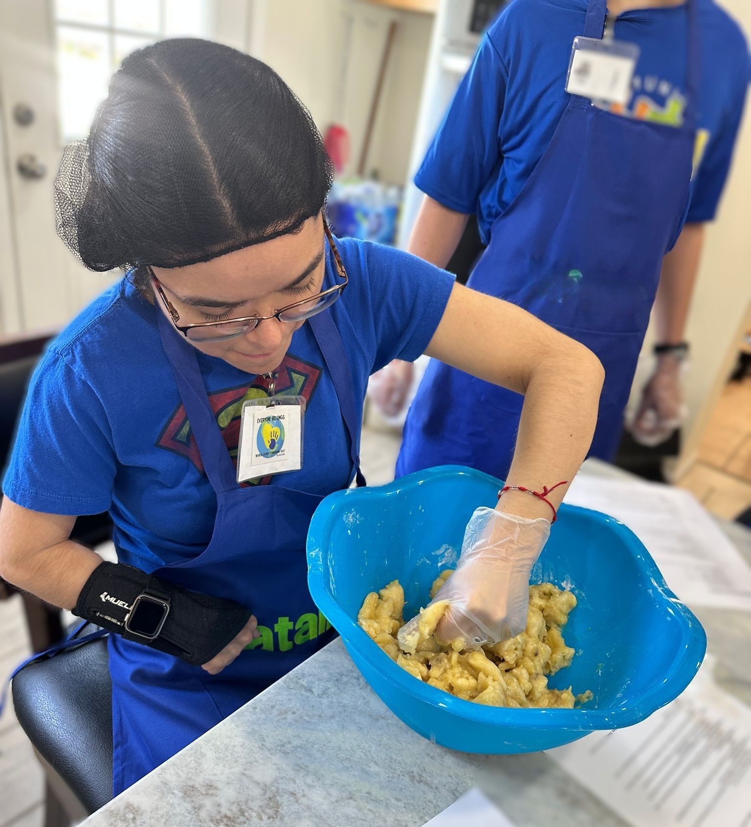 A woman in a blue apron mixing food in a blue bowl