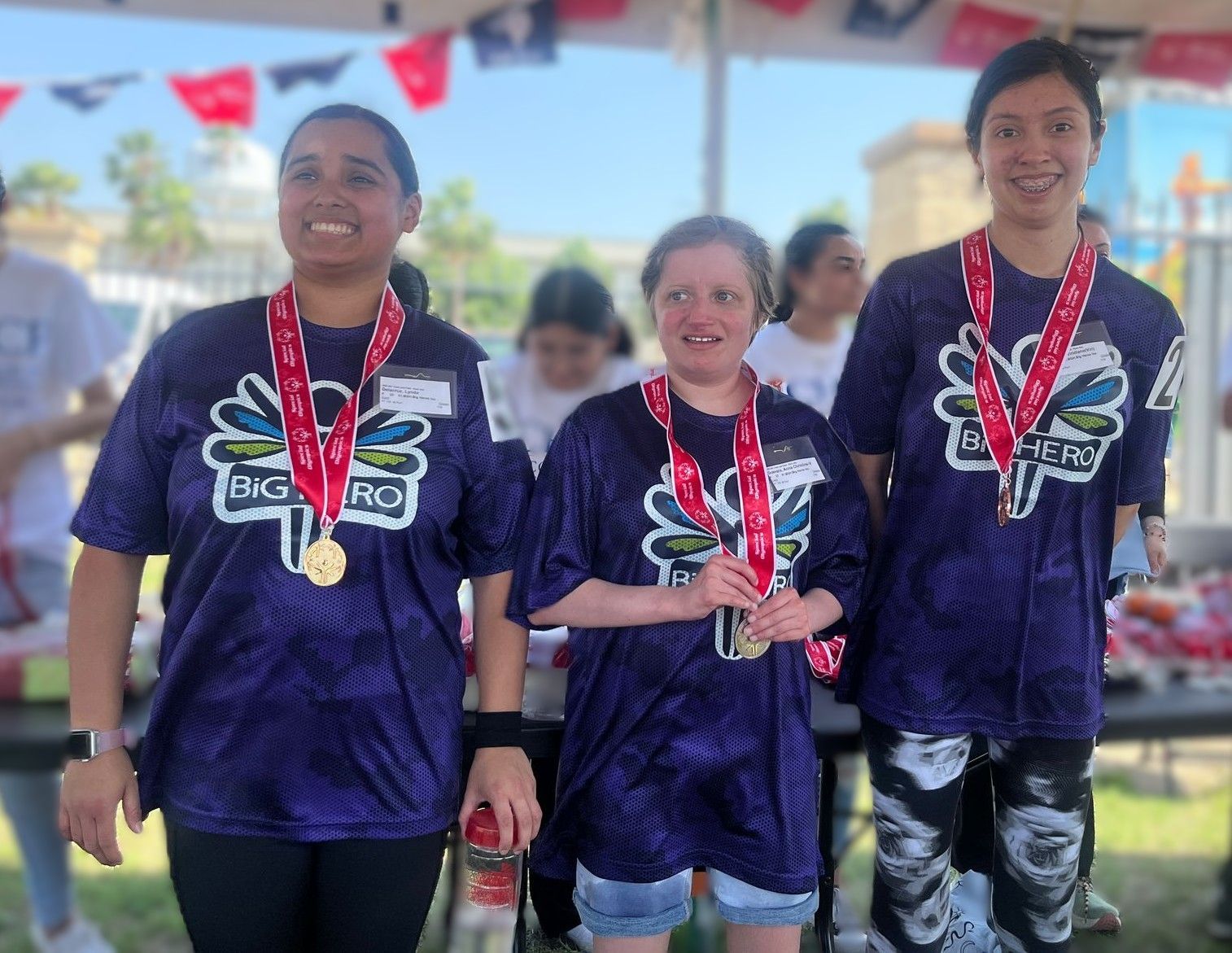Three girls wearing purple shirts and medals are standing next to each other.