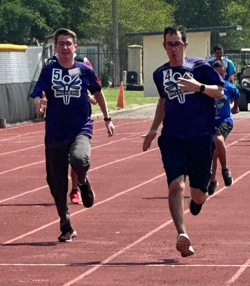 Two men are running on a track and one has the number 5 on his shirt