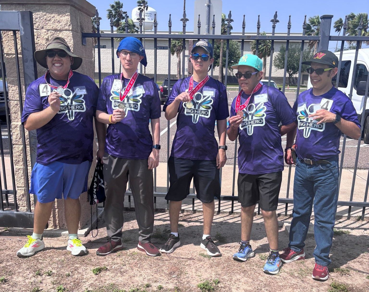 A group of men wearing purple shirts and medals are standing in front of a fence.