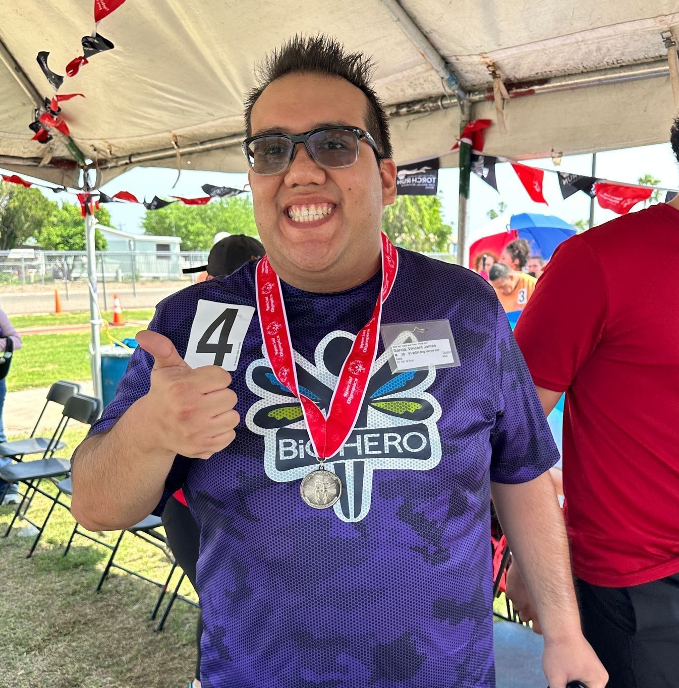 A man wearing a purple shirt that says big hero gives a thumbs up