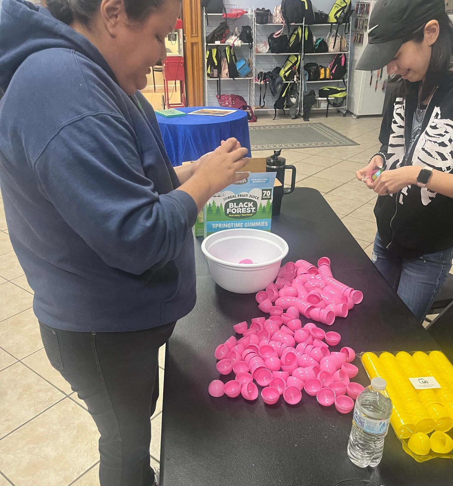 Two women are sitting at a table with a bunch of pink cups and a bottle of water