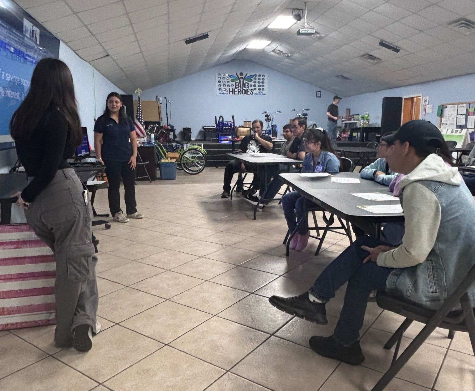 A woman stands in front of a group of people sitting at tables