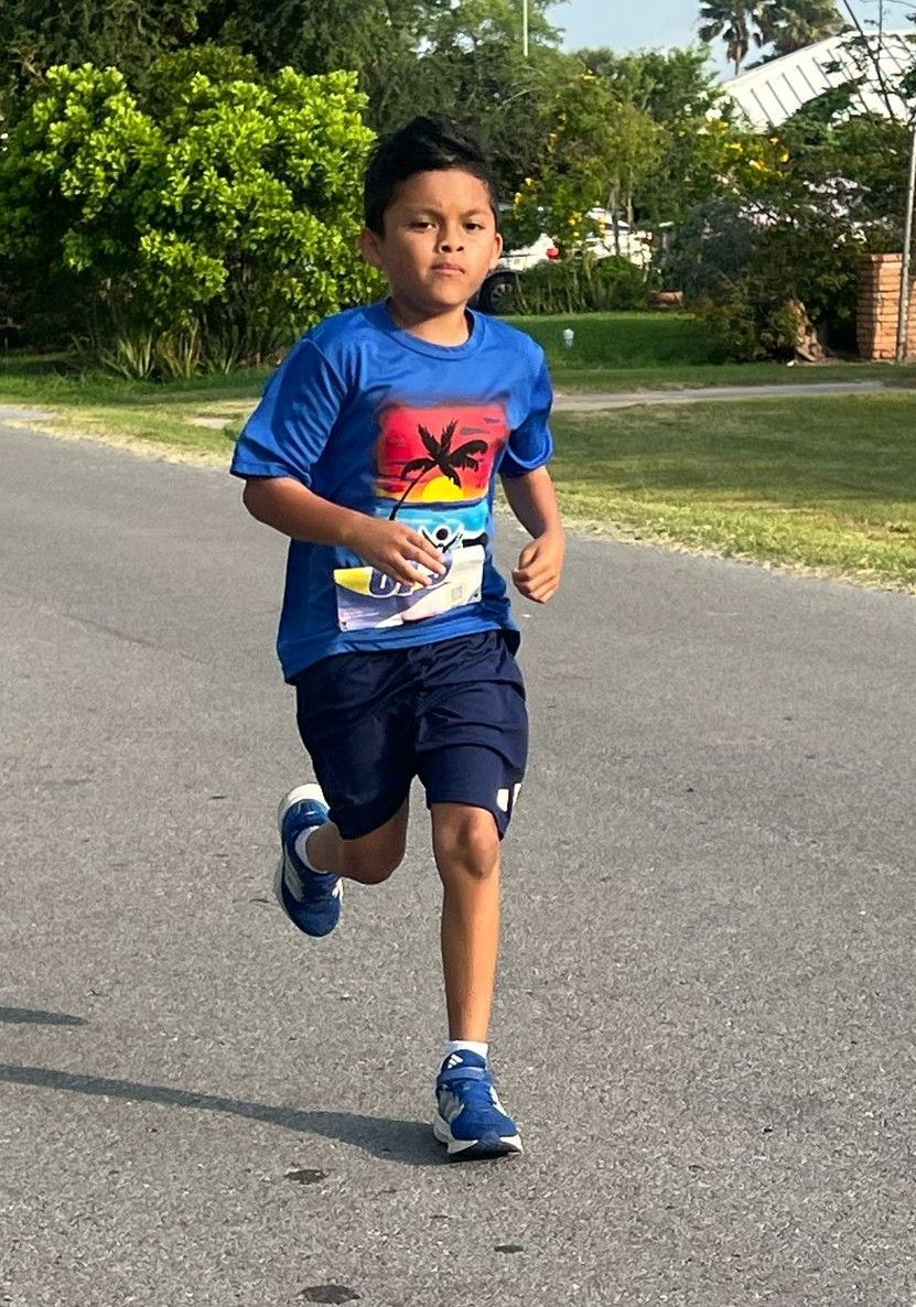 A young boy in a blue shirt is running down a road.