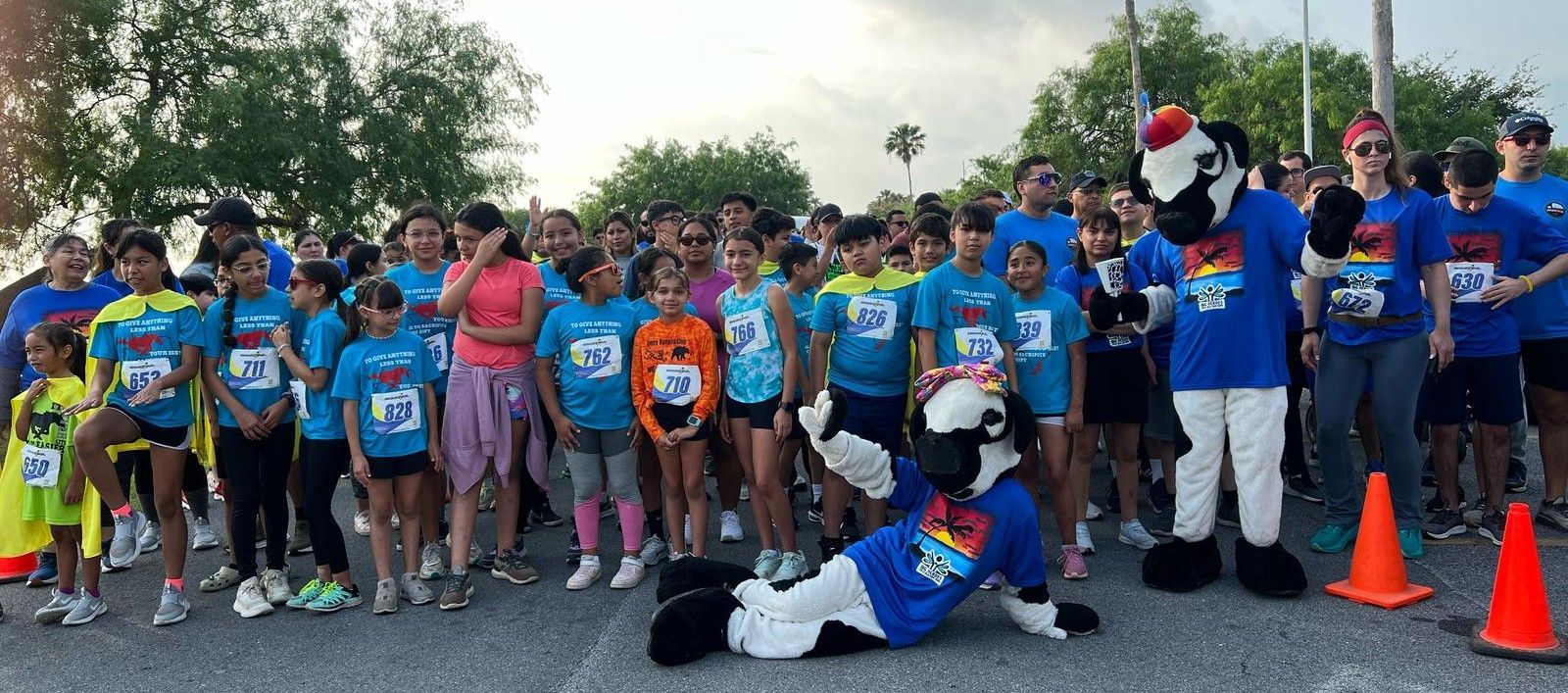 A group of children and mascots are standing in a parking lot.