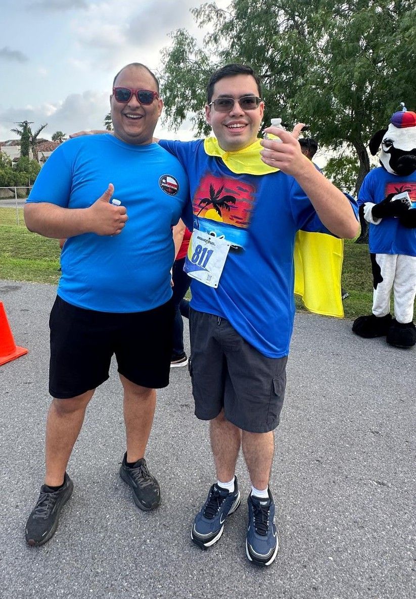 Two men posing for a picture with one wearing a bib that says 891