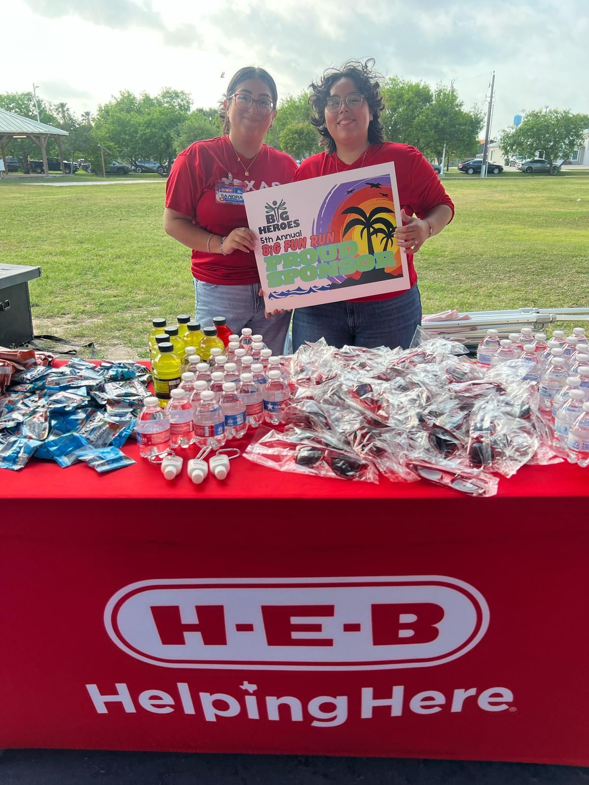 Two women are standing in front of a table that says h-e-b helping here