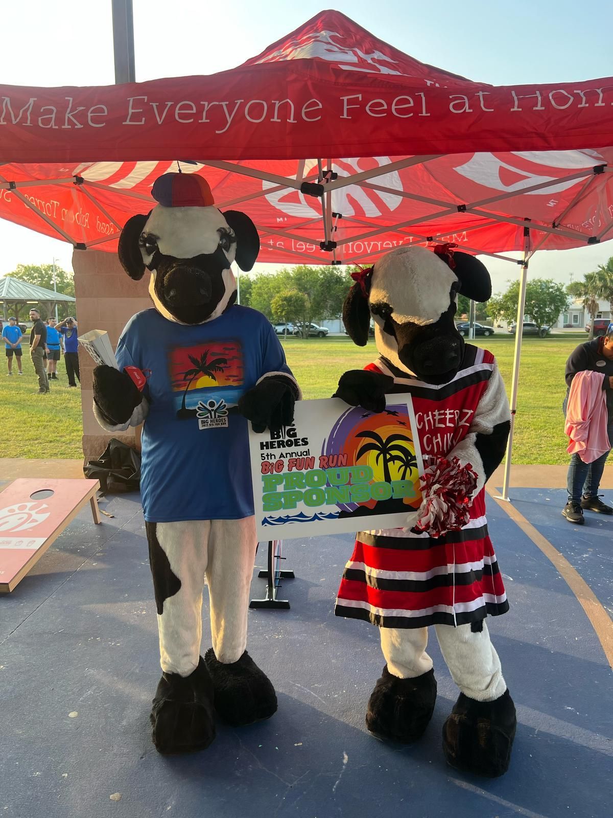 Two mascots are standing under a tent that says make everyone feel at home