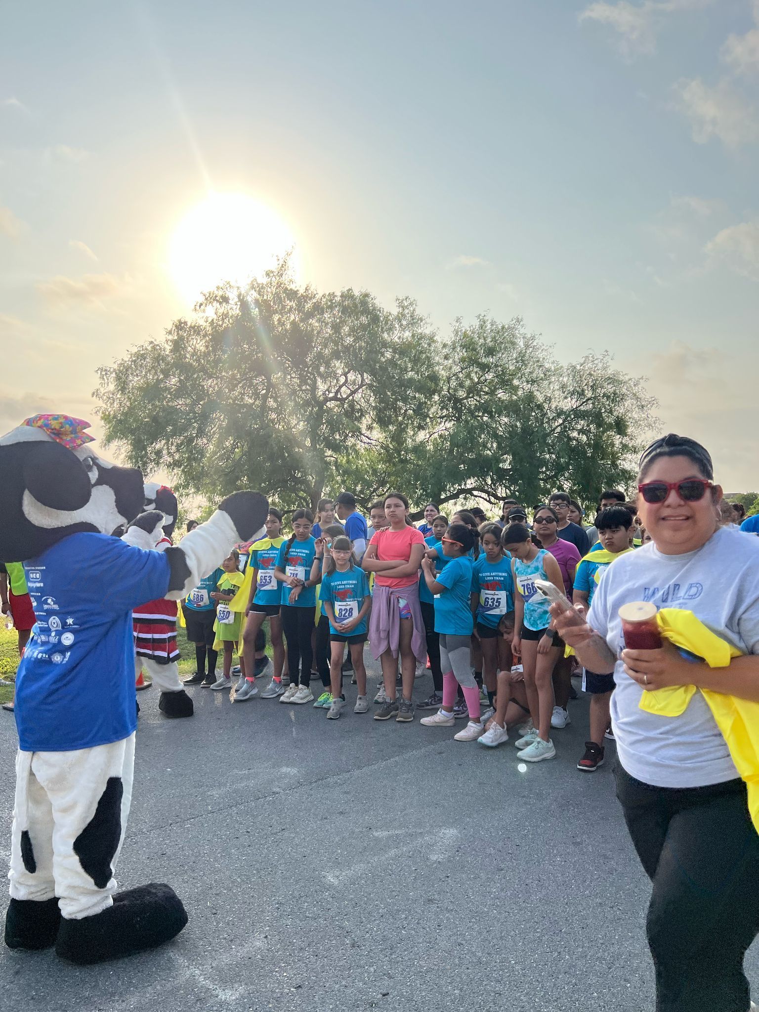 A cow mascot is standing in front of a crowd of people