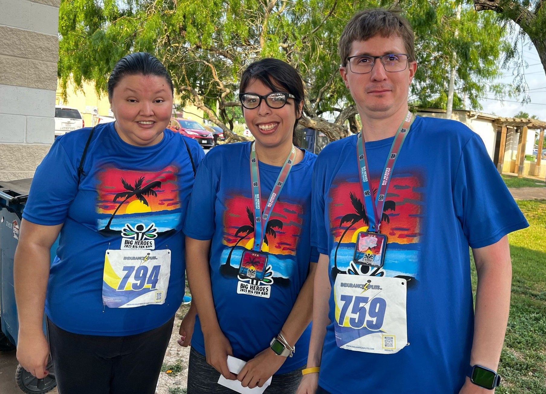 Three people wearing blue shirts with palm trees on them are posing for a picture.