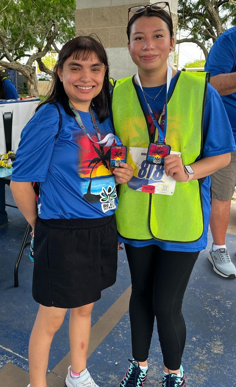 Two women in blue shirts and yellow vests are posing for a picture.