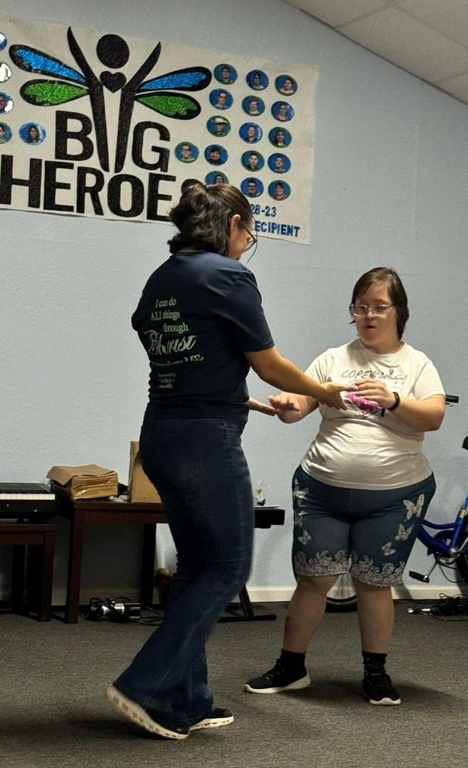 Two women are dancing in front of a sign that says big heroe