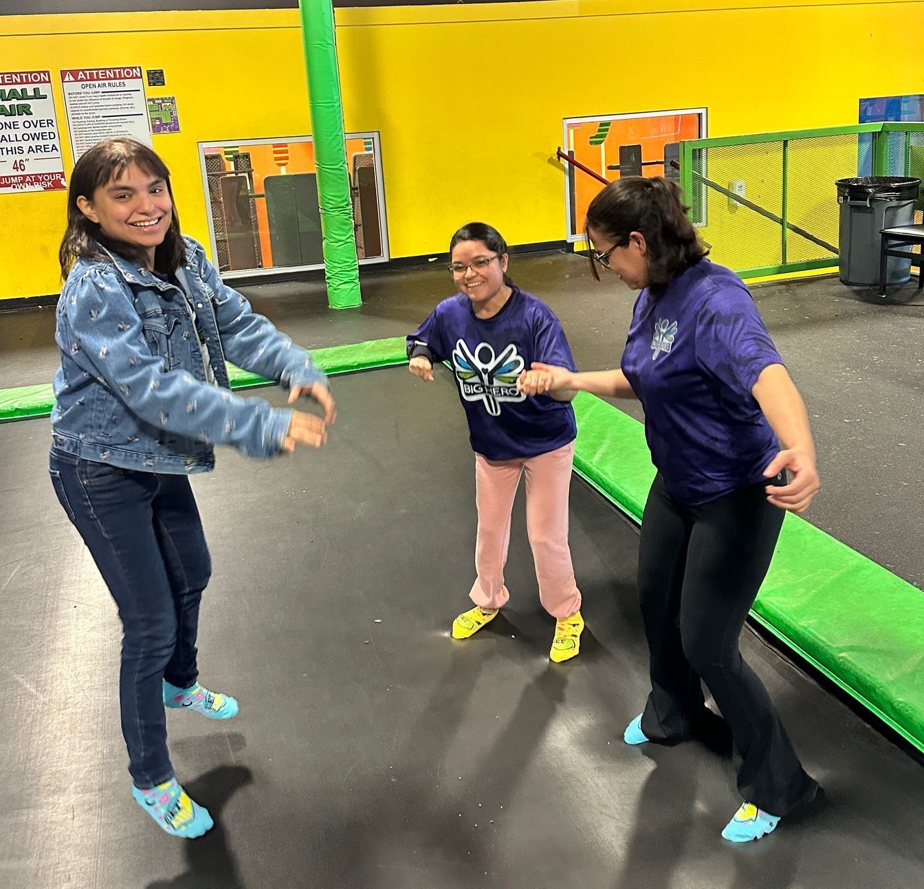 Three women are playing on a trampoline with one wearing a shirt that says aoa