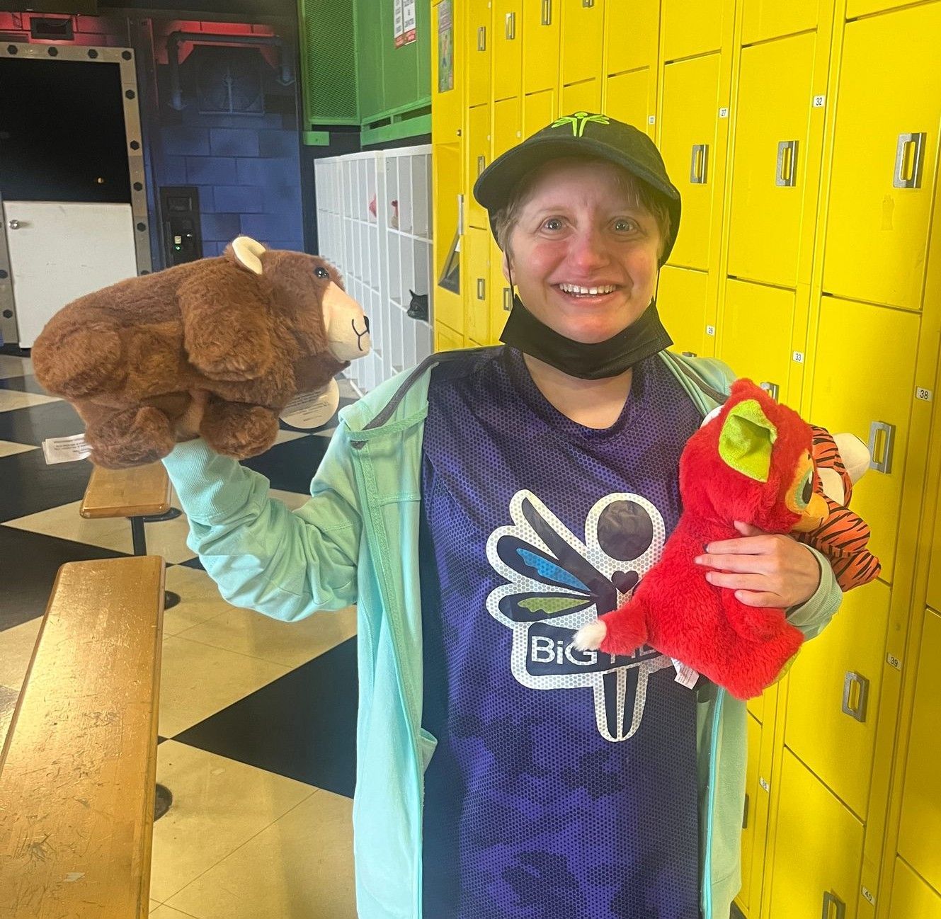 A woman holding two stuffed animals in front of yellow lockers