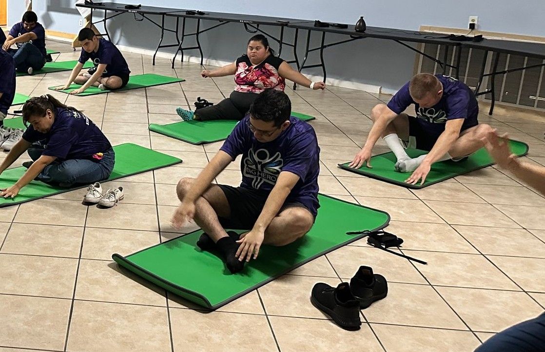 A group of people are sitting on green yoga mats in a room.