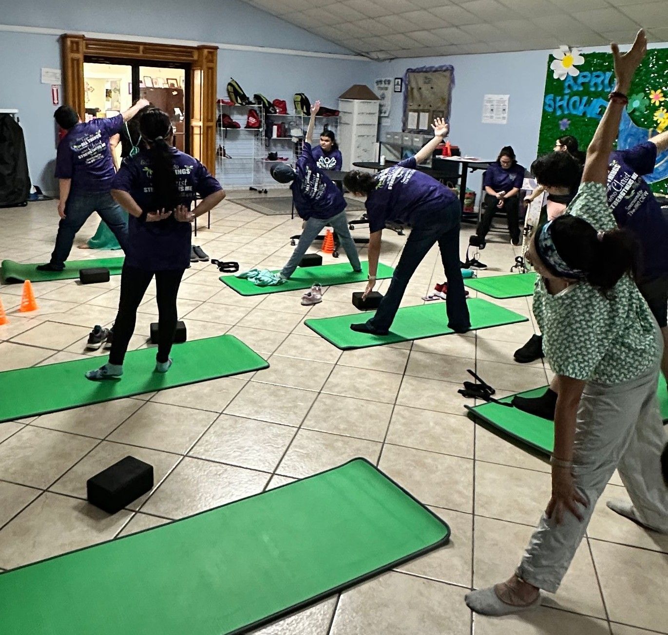 A group of people are doing stretching exercises on green mats