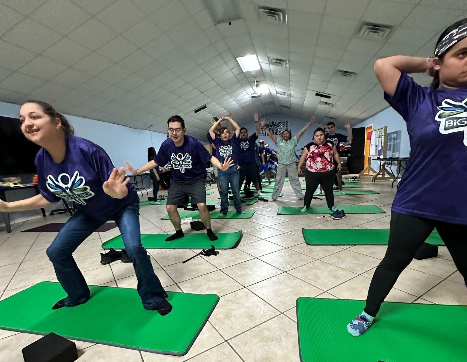 A group of people are doing yoga on green mats in a room.