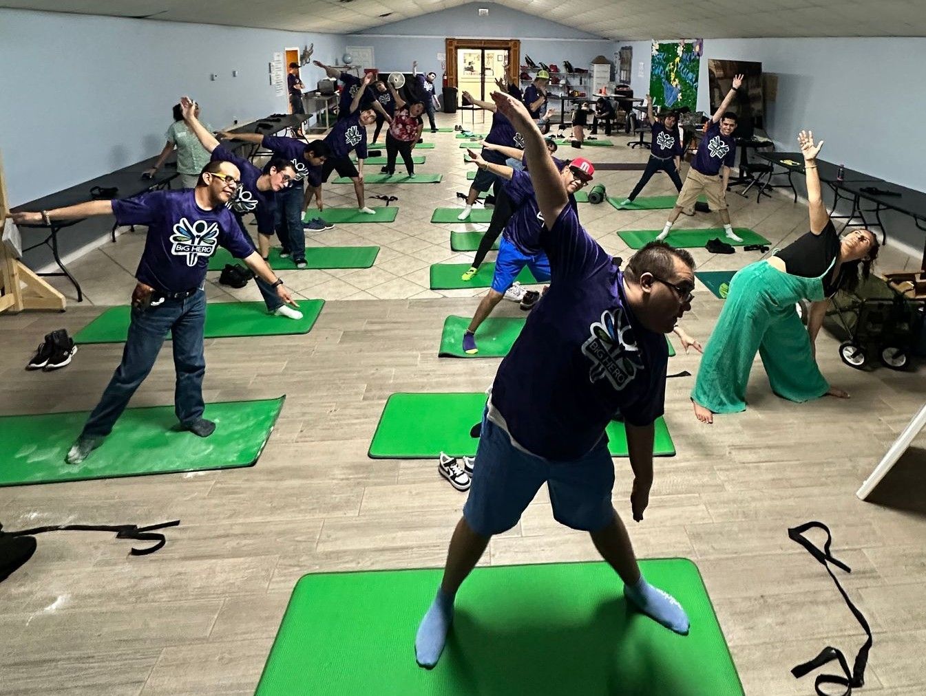 A group of people are doing yoga on green mats in a room.