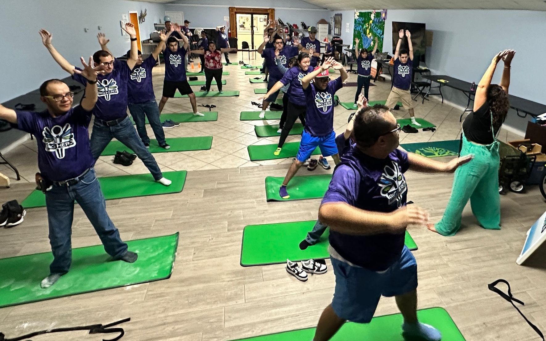 A group of people are doing yoga on green mats in a room.