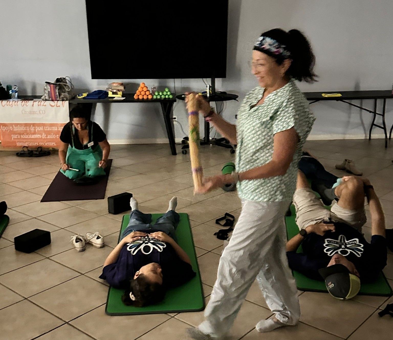 A woman is standing in a room with people laying on green mats