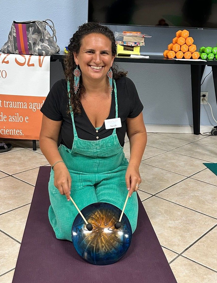 A woman is kneeling on a yoga mat playing a gong