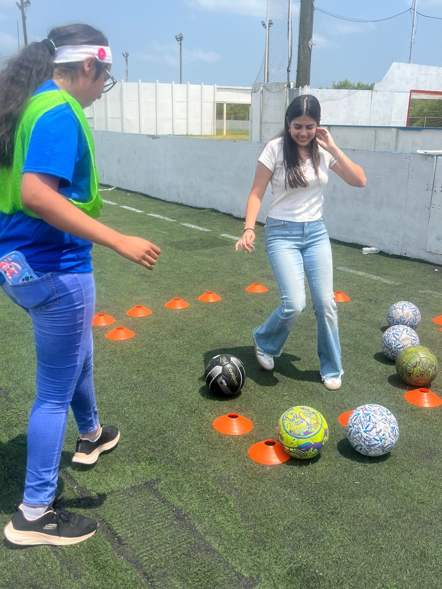 Two girls are playing soccer on a field with cones and balls