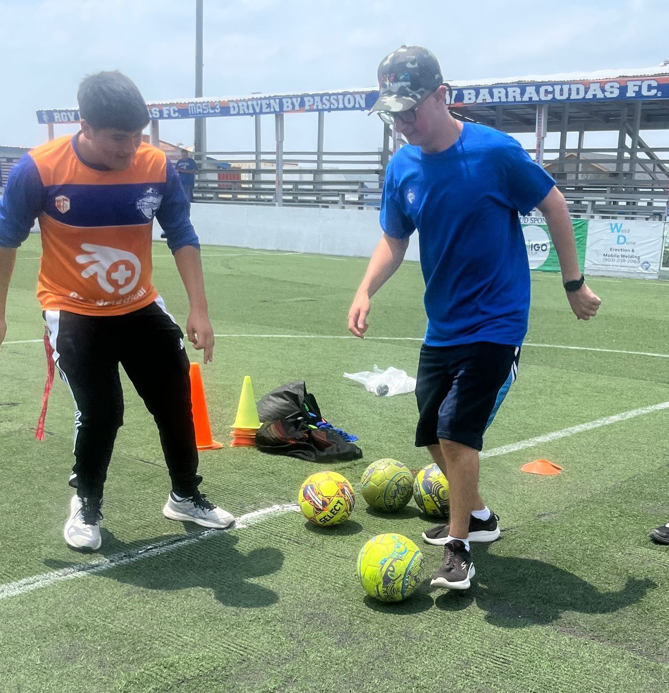 Two men playing soccer in front of a sign that says barracudas