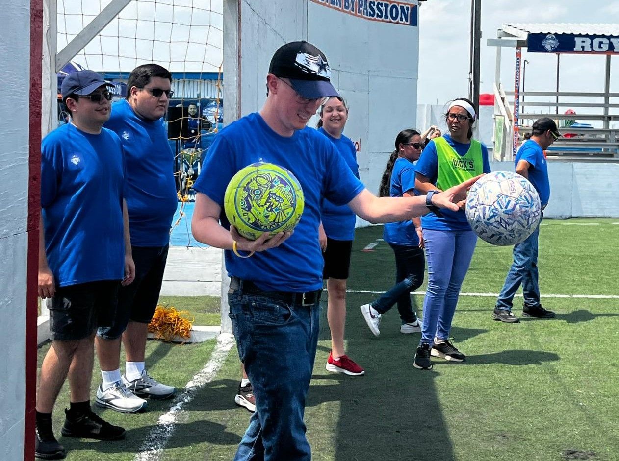 A man in a blue shirt is holding a soccer ball in front of a group of people.