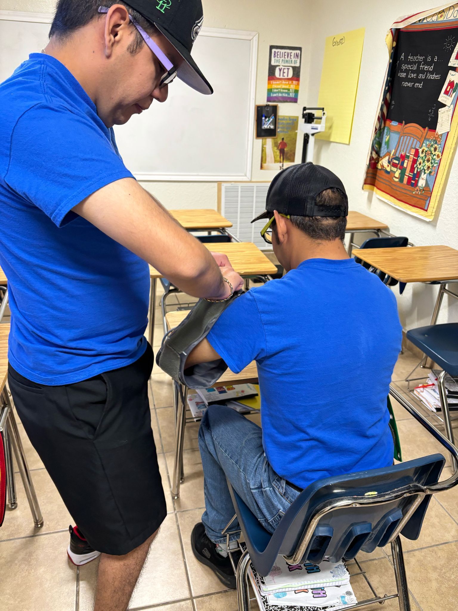 A man in a blue shirt is helping another man in a classroom