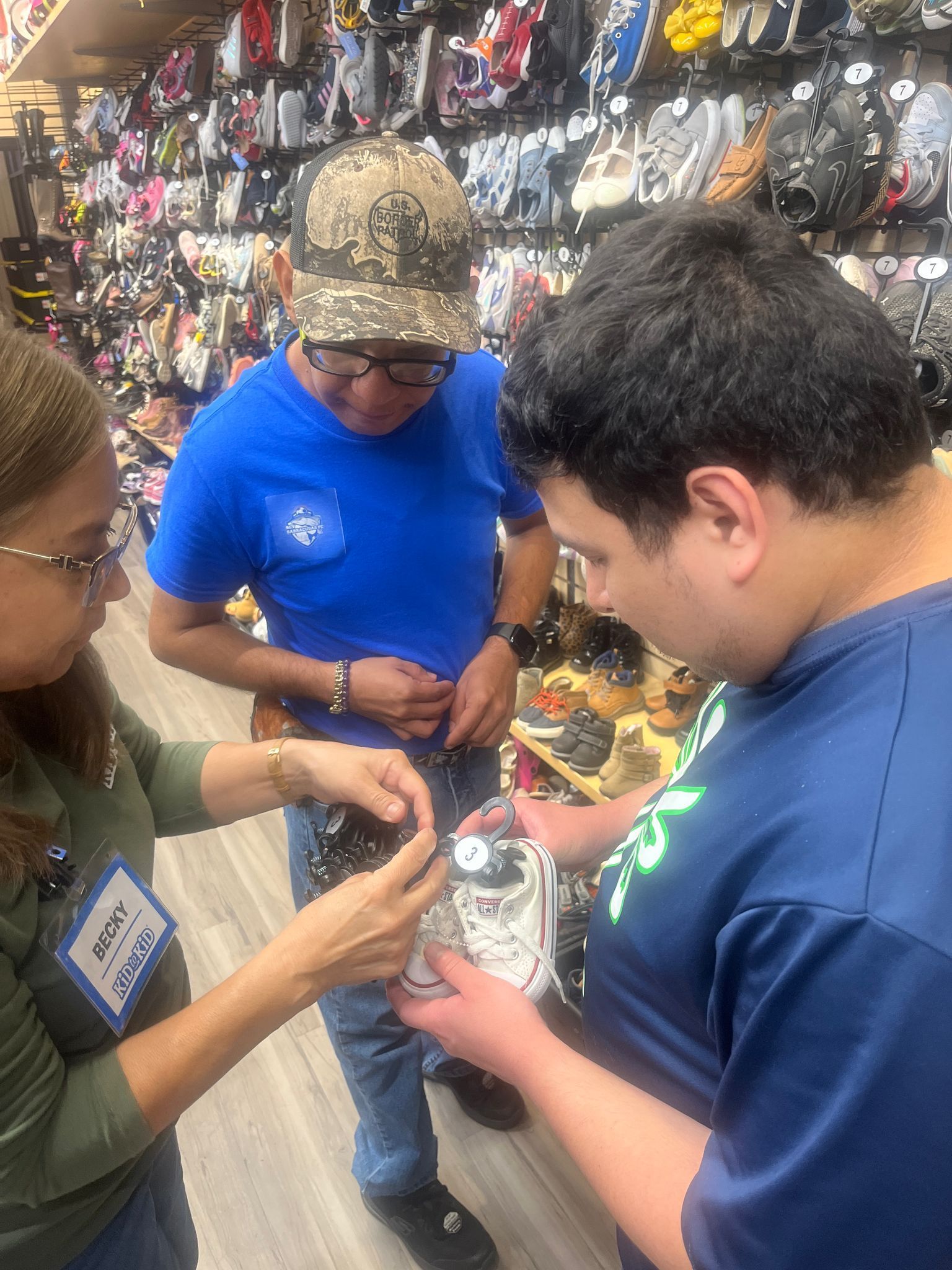 Three people shopping for merchandise at a store. Two people looking at the merchandise held by another person.