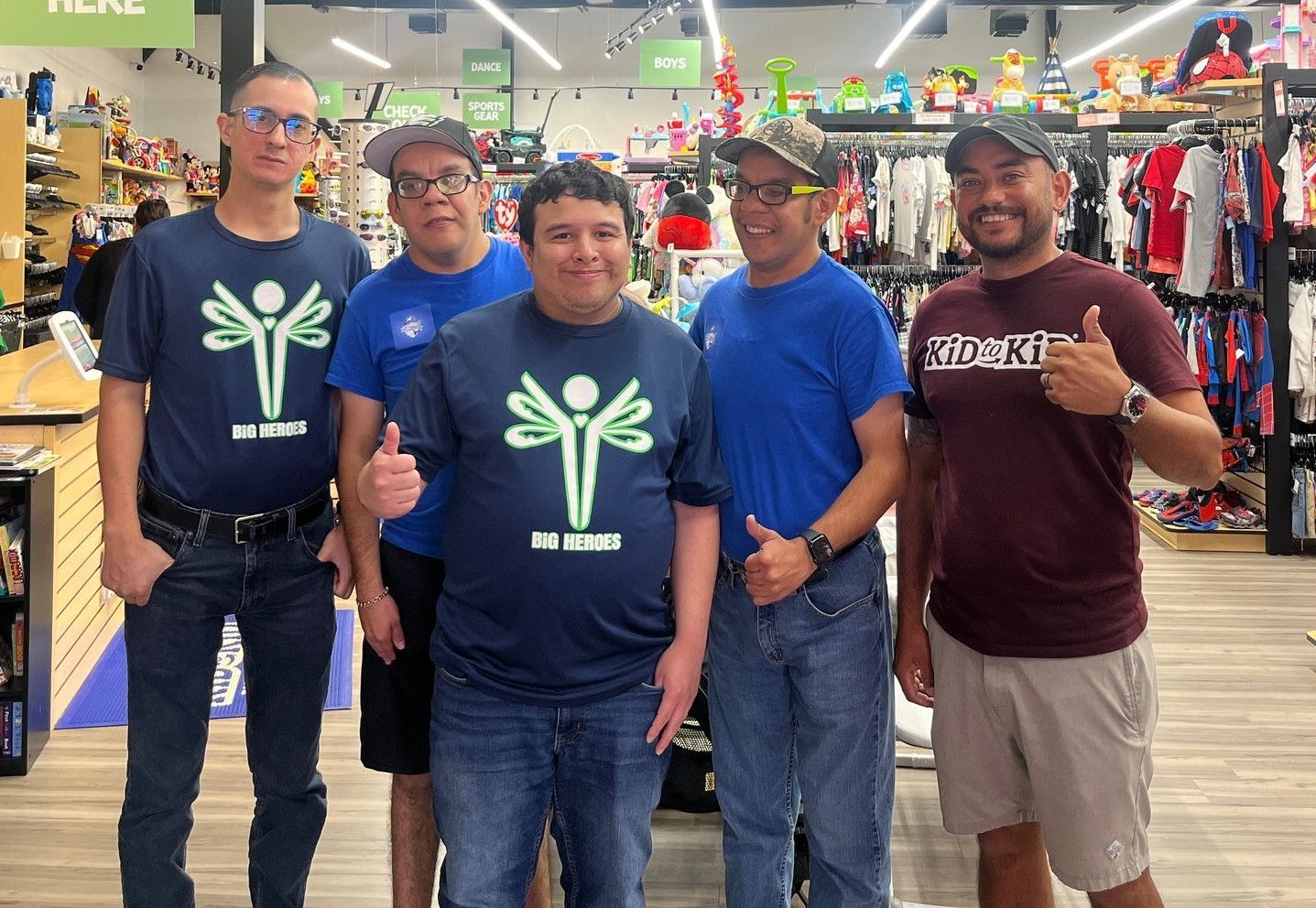 Five people in a store, wearing matching shirts, give thumbs up.