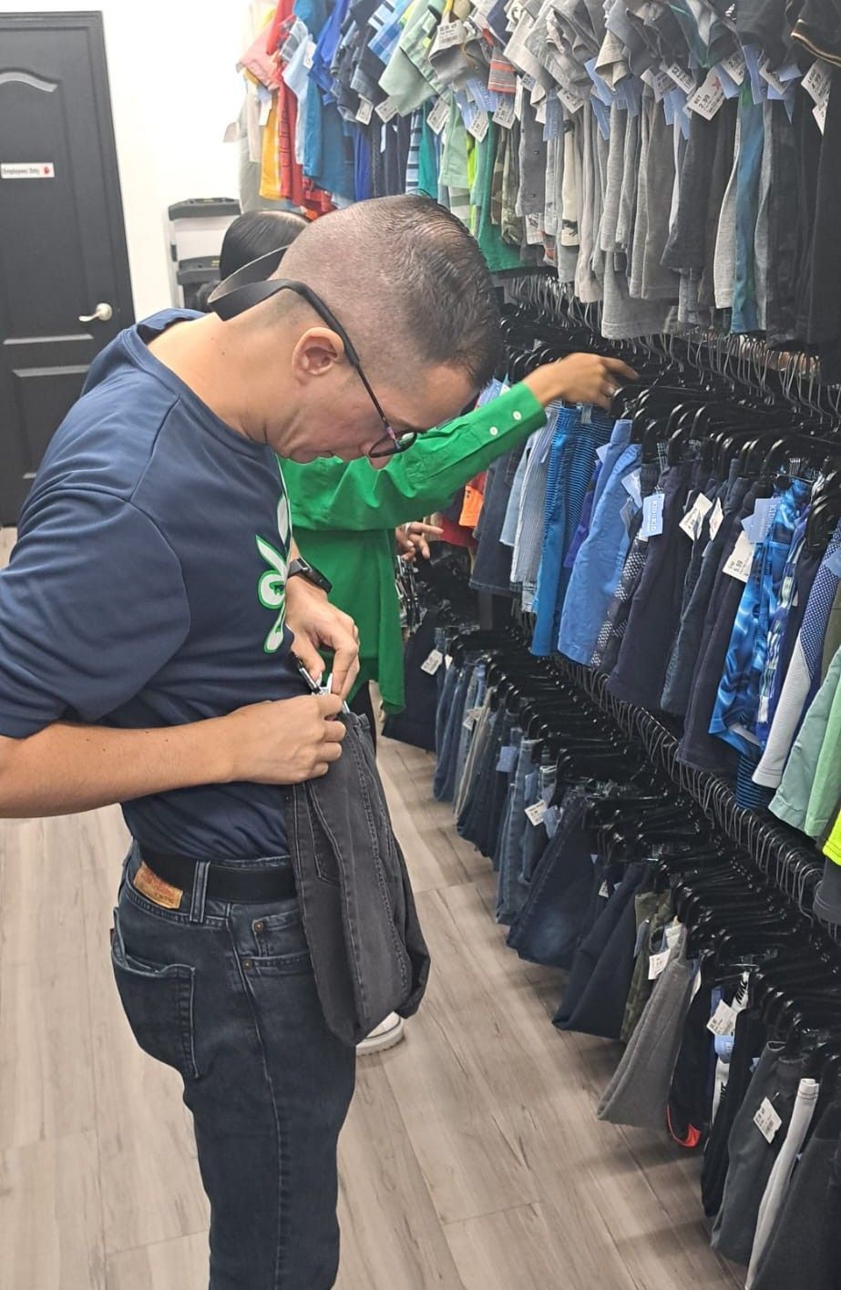 Man in a clothing store looking into his pocket, clothing racks in the background.