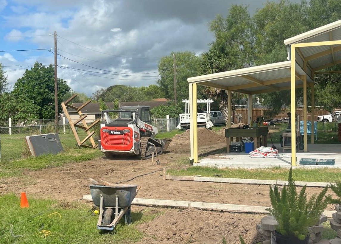 A bulldozer is driving down a dirt road in front of a house under construction.