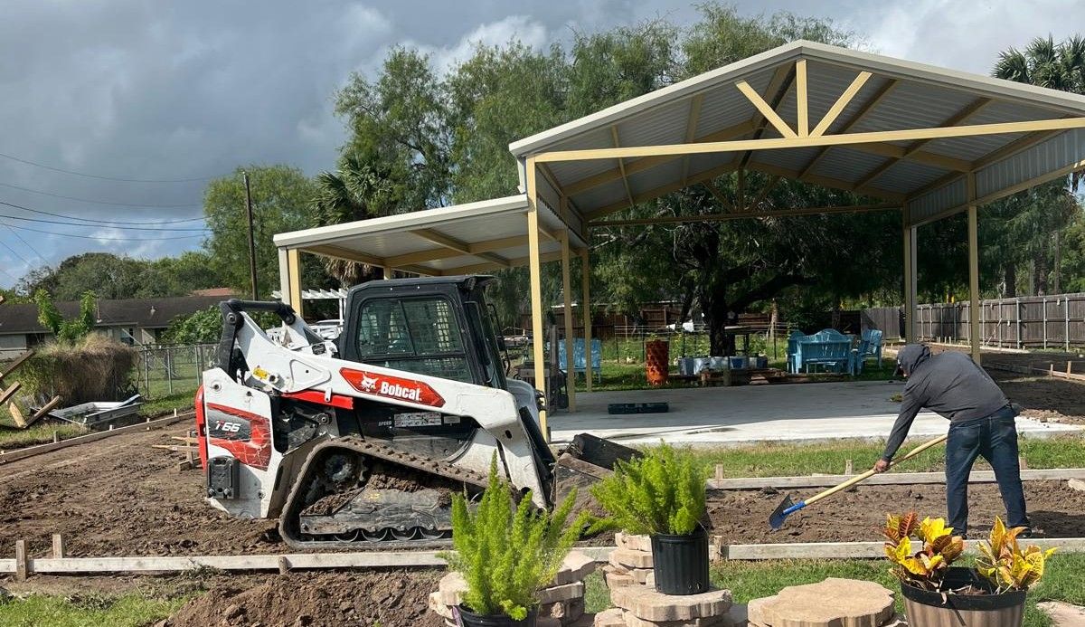 A man is working in a yard with a bulldozer in the background.