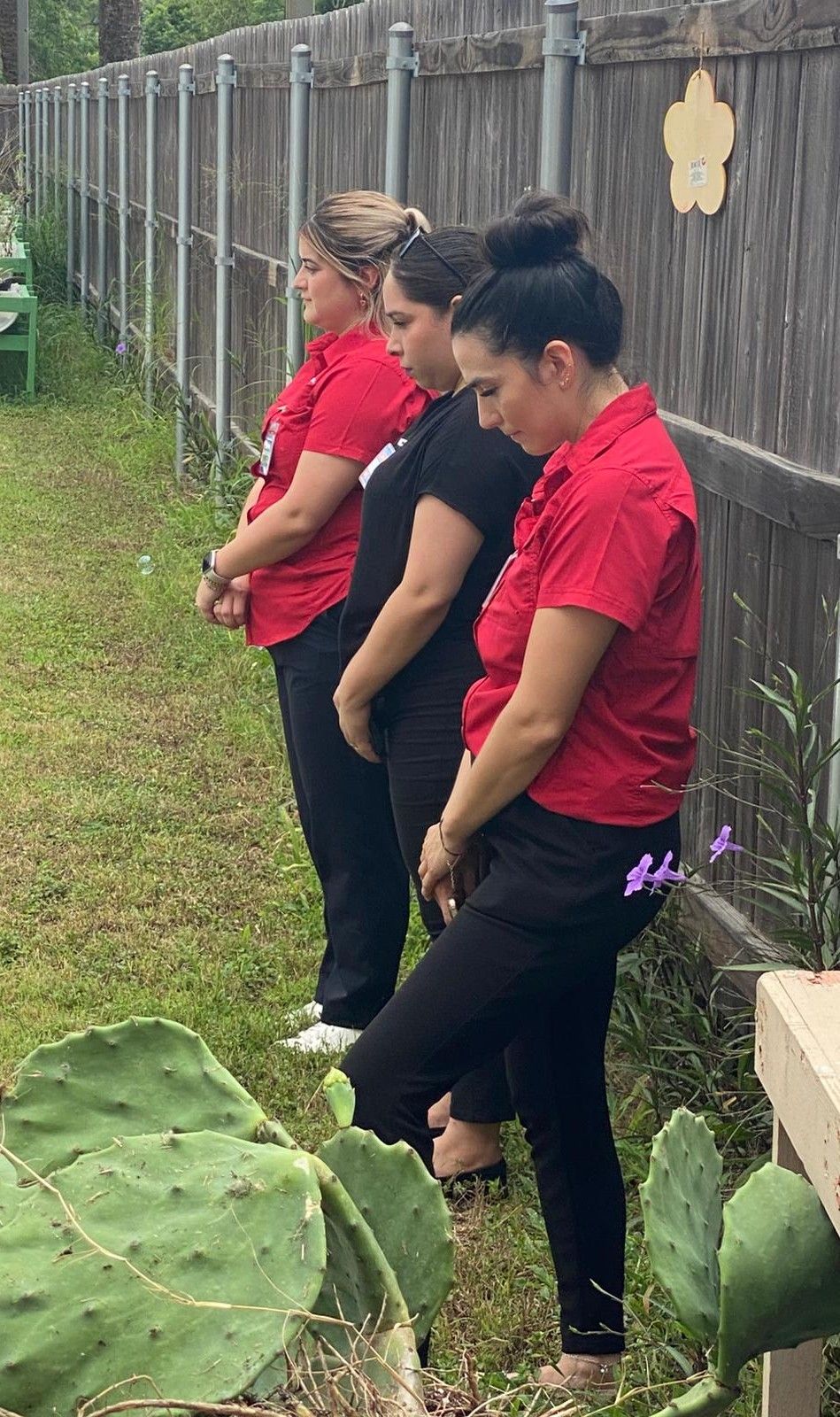 Three women are standing next to each other in front of a fence.