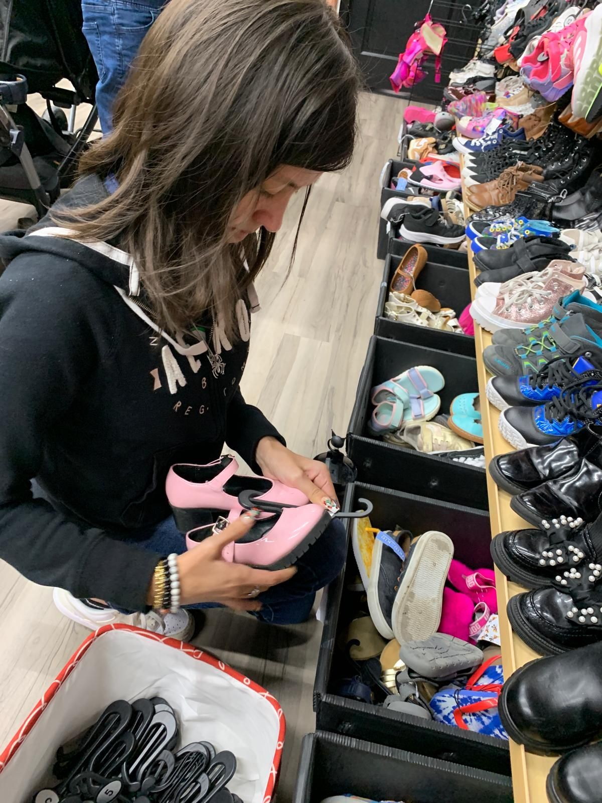 Woman looking at pink shoes in a store. She wears a black hoodie, and other shoes fill the shelves.