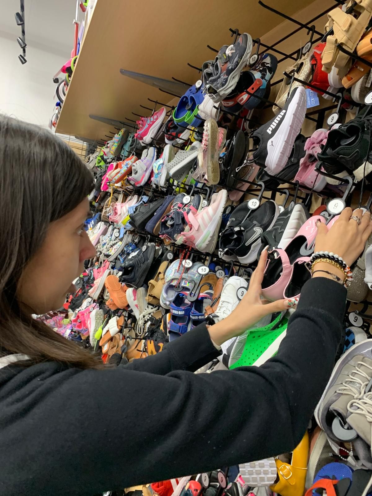 Woman browsing shoes on display at a retail store, reaching toward a pair.