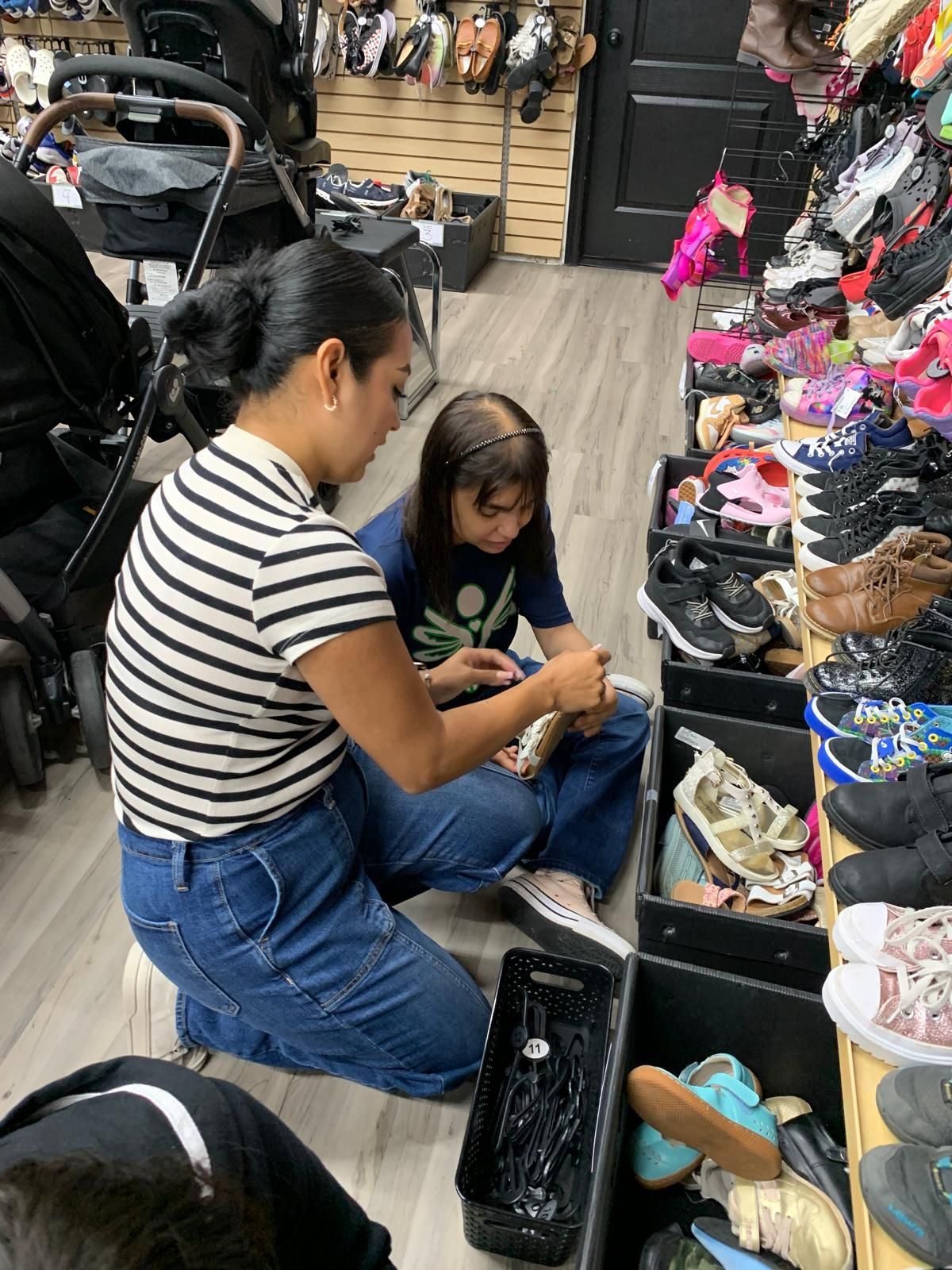 Woman helping child select shoes in store. Both are kneeling by shoe display.