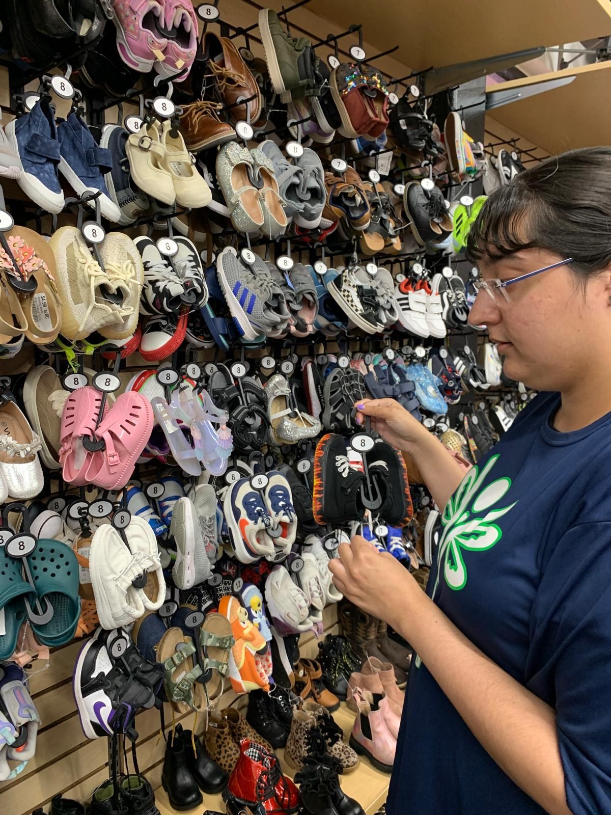 Woman browsing a wall of shoes in a store, selecting a pair with a Mickey Mouse design.