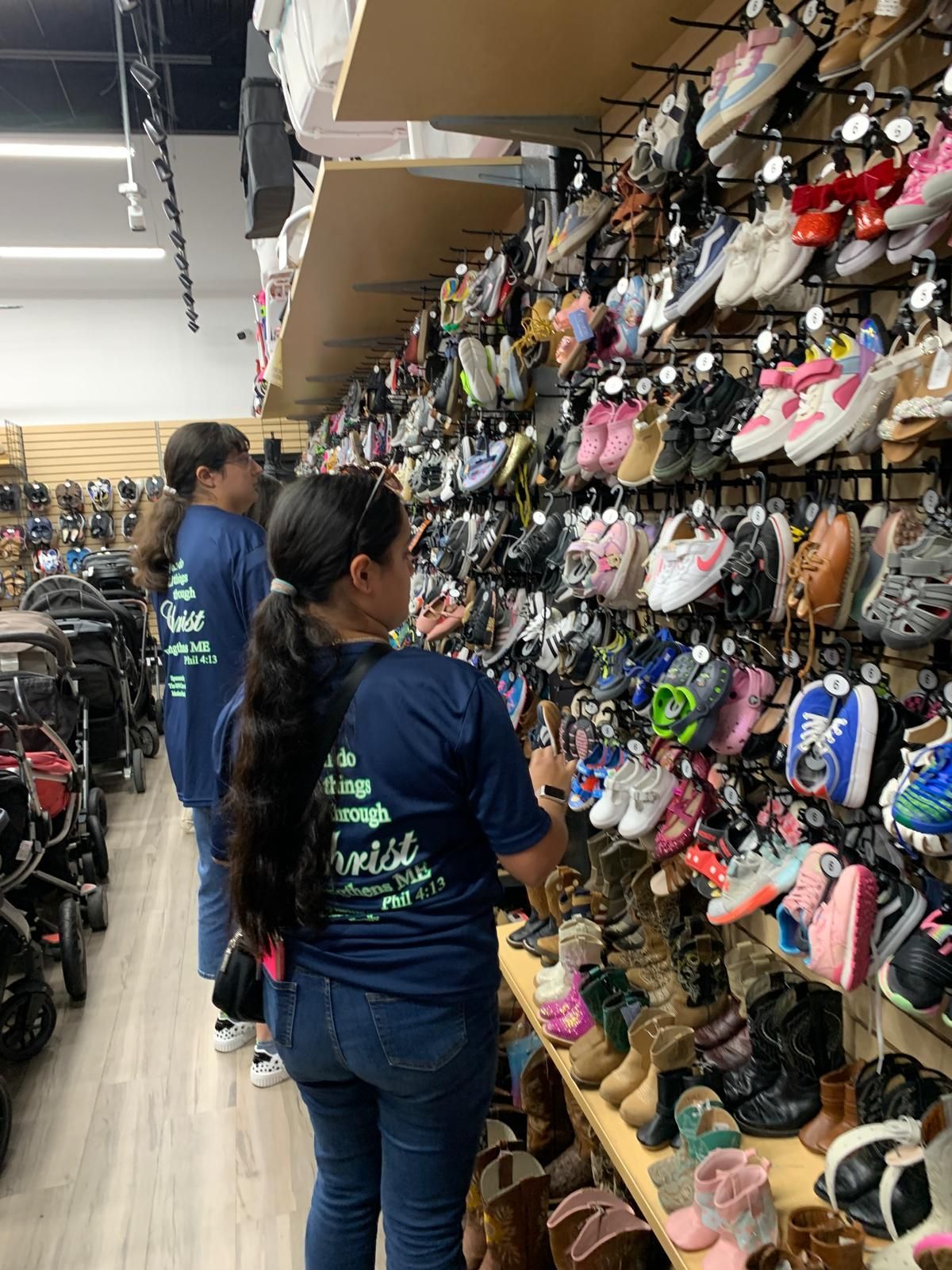 Two women looking at shoes on a wall display in a brightly lit shoe store.